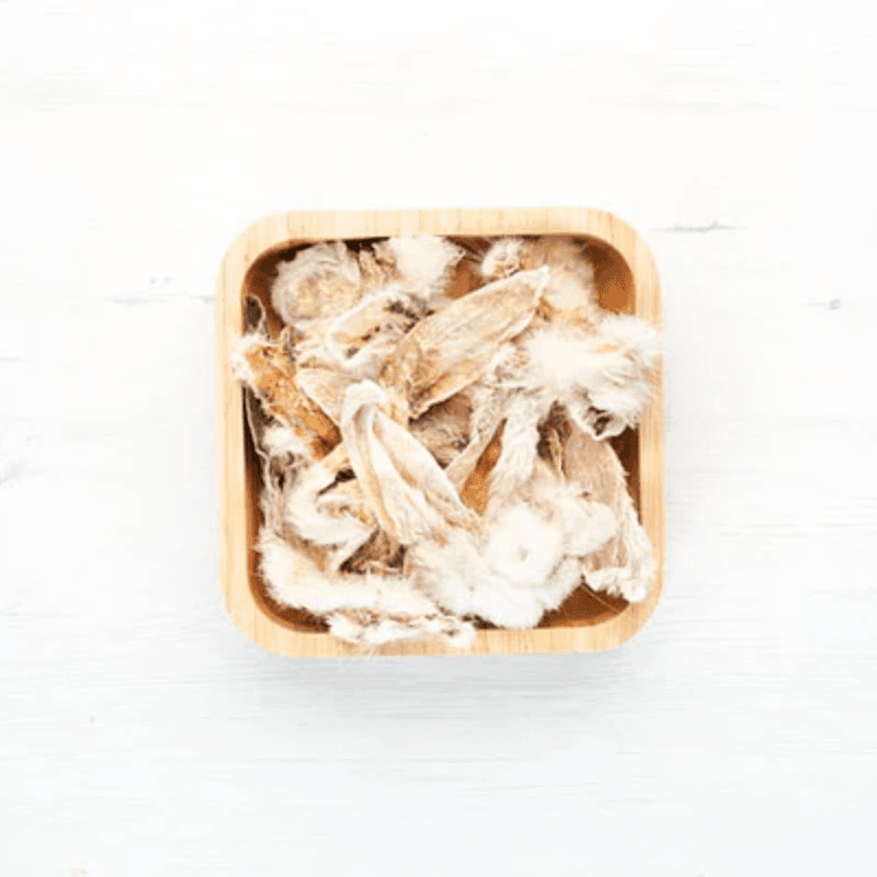 Orejas de conejo con pelo deshidratadas en un recipiente de madera, snack natural para perros.